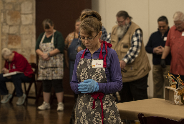 Volunteer helper Jan Phillips bows her head for a prayer offered by Reverend Dr. Roger Clayton, pastor at  Georgetown's St. John's Methodist Church during the Community Thanksgiving, held at the Georgetown Community Center in San Gabriel Park on Thursday, November 23, 2023.