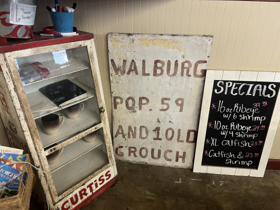 , An old sign shows Walburg’s population, including “1 old grouch,” jokingly noting the space’s previous owner. 