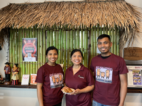 Elsie Corass, owner of Elsie’s Egg Rolls in Hutto, stands holding an eggroll order next to her two children, Reina Lamberton and Eugene Trinidad. The order counter behind them is modeled after a traditional Nipa Hut. Photo by Abbey Archer