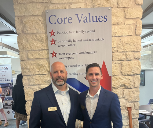 Bryan Chisholm and Michael Pickel stand in front of a sign displaying their core values. 