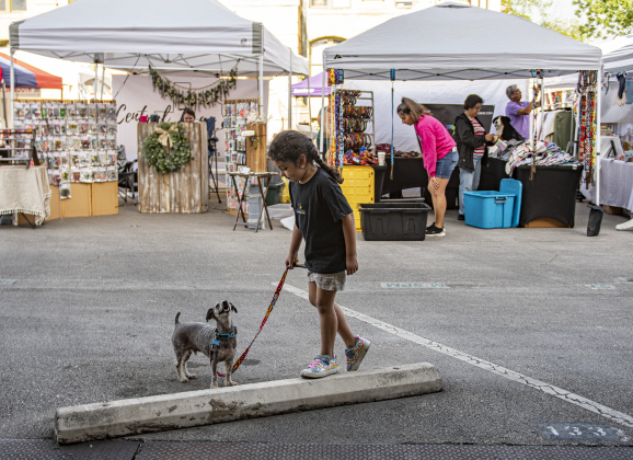 5-year-old Natalia Reyes spends time with Chino, her 11-year-old family pet while mom Itzel Rincon  (in back, wearing pink shirt) puts things in place at her booth for Azteca Pet Mexican-Artisan  during Market Days, held Saturday, April 13. Photo by Andy Sharp