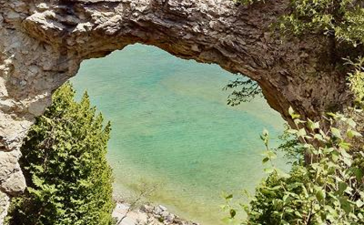 “Bicycle Arch” photograph by Ellen Greeney captures a lone biker riding in Mackinac Island State Park in Michigan on Lake Huron. The Arch Rock is nearly 15 stories tall of natural limestone. Photo by Ellen Greeney