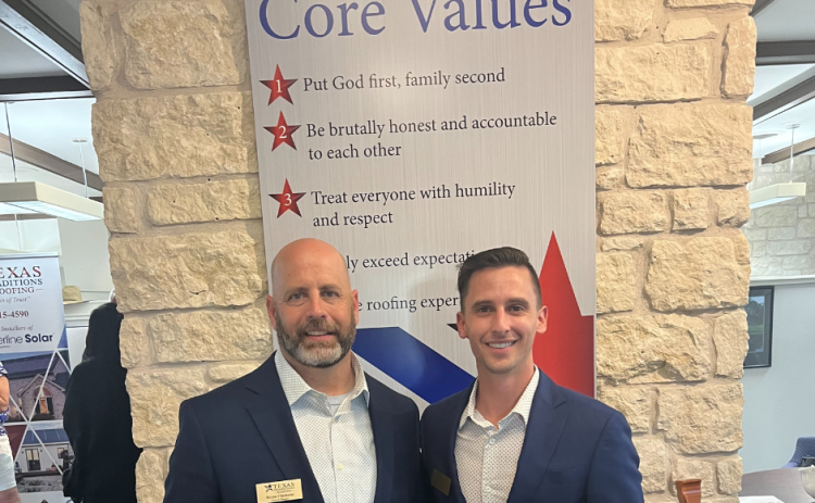 Bryan Chisholm and Michael Pickel stand in front of a sign displaying their core values. 