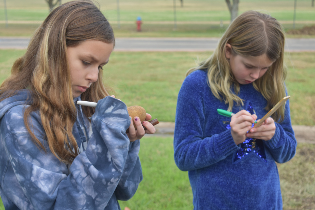 Students Hannah Rimel and Ainsley Kirk write peace sentiments on garden rocks and sticks.