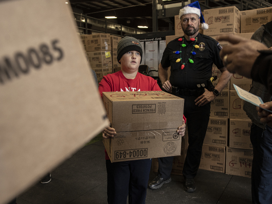 Volunteer Fletcher Robey, 10, waits for instructions on where to hand out a gift box  to recipients  under the watchful eyes of Georgetown Police Chief Cory Tchida, back right.