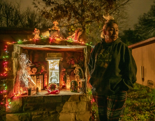 San José neighborhood resident Alma Espinoza is pictured on Tuesday, December 20, 2022 as she  stands next to a tribute to her daughter Alexandra Chavarria, who died in a car accident on Interstate 35 one year ago .