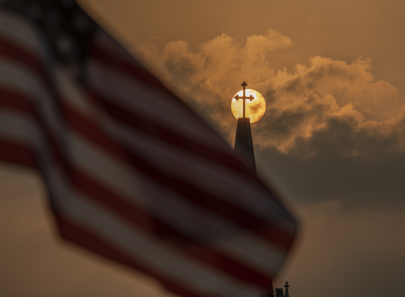 An American flag waves in the evening wind along West Davilla Street as the sun goes down beyond Saints Cyril and Methodius Catholic Church  on Thursday, May 11, 2023, the opening night of Lakefest in downtown Granger.