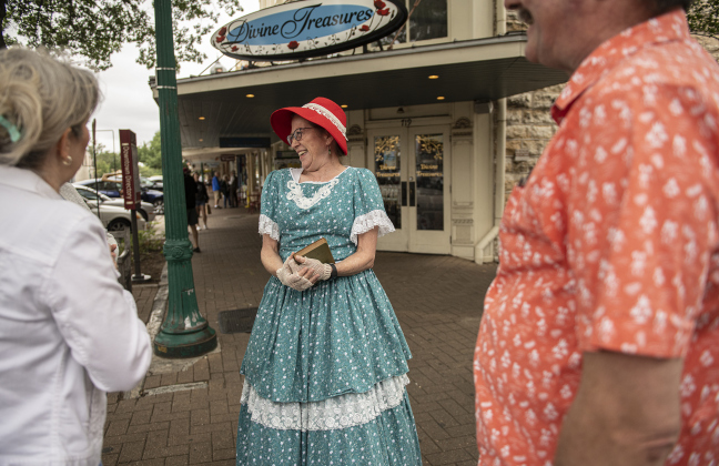 Docent Robin Lingren, dressed as Lula Holland Leavell, stands at the corner of 8th and Main Street as she speaks with Heather and Ed Penniman.