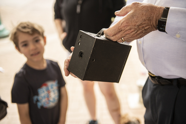 7-year-old James Stasik, left, looks on as docent Jerry McCalley, in the role of photographer Robert Stone, talks about a vintage early-1900s-era Kodak Brownie 2a camera. Stone had an upstairs studio at 8th and Main Streets.