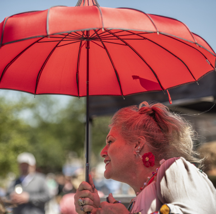 Tammy Hogue uses a parasol to hold back the sun's rays.  Hogue made her poppy earrings the night before the festival.