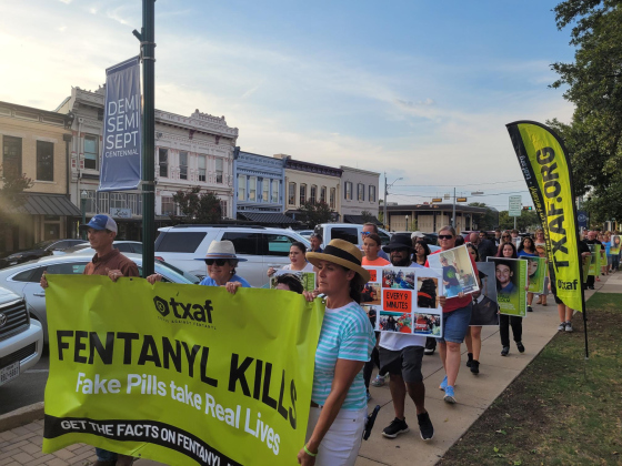 Adam Crump, left, Williamson County Precinct 1 Commissioner Terry Cook, center, and Justice of the Peace Angela Williams, Precinct 2, carry a banner and lead the August 21 Fentanyl Awareness walk around the county courthouse. Photo by Nalani Nuylan.