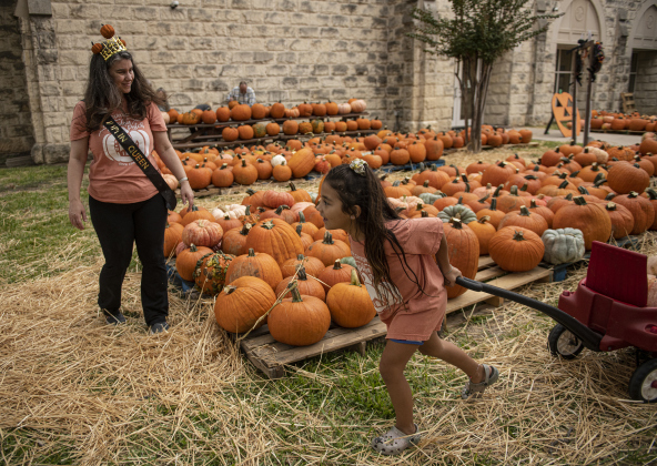 Honey Habingreither, left, the church's designated Pumpkin Queen, looks on as 7-year-old Teddi Perez, right, gets ready to place pumpkins.