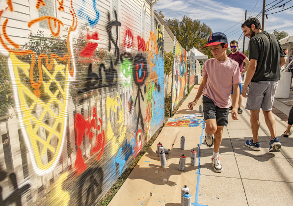 11-year-old Jace Chisnell looks for a good place to add spray paint creations to a mural at the South Main Arts Festival on Saturday, October 21, 2023.  Josh Macias, behind Jace at right (in dark shirt), a staff member at the Georgetown Public Library, came up with the mural idea for the festival.