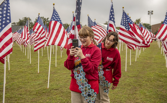 Virginia Lubrano, 15, left, and her sister Eliza, 16, members of American Heritage Girls Troop 2911, take photos of themselves while helping place  American flags at the Field of Honor on Saturday, November 4, 2023.