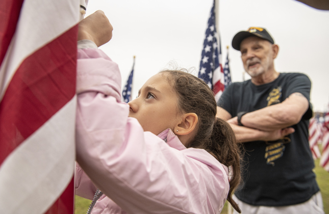 8-year-old Lourdes Aviña places a name tag on a flag under the watchful eye of Vietnam veteran Mike Wright  at the Field of Honor on Saturday, November 4, 2023. 