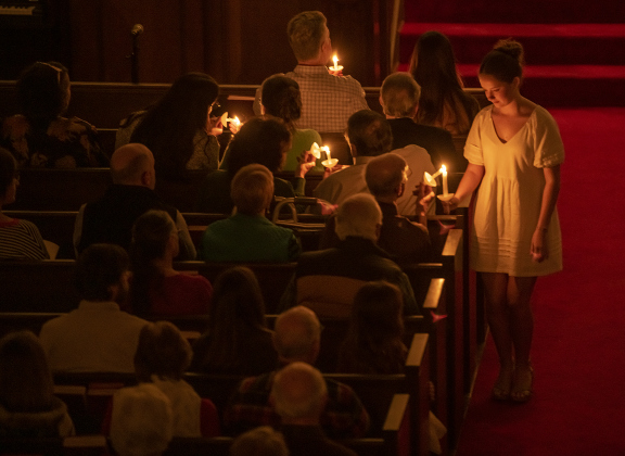 An usher helps light candles for  attendees during Southwestern University's Candlelight Service at Lois Perkins Chapel on Thursday, December 7, 2023.