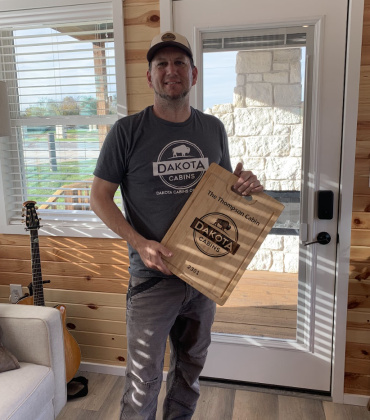 COO, Aaron Thompson holds a custom cutting board that Dakota Cabins customers get when they receive their cabin. (Photo by Kaitlyn Wilkes)
