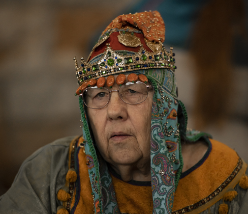 Regina de Masquer was dressed in brightly-colored clothing during a meeting of The Stellar Kingdom of Ansteorra.