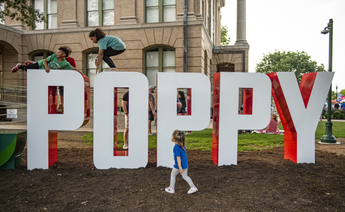 Children enjoy playing on the large Poppy letters on the courthouse lawn along 8th Street on the opening night of the Red Poppy Festival on Friday, April 26.  Photo by Andy Sharp