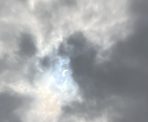 The partially eclipsed sun peaks through the clouds.