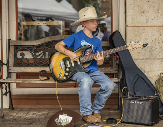 8-year-old Max Fomchev plays his guitar along Main Street during the 25th Annual Red Poppy Festival on Saturday, April 27.