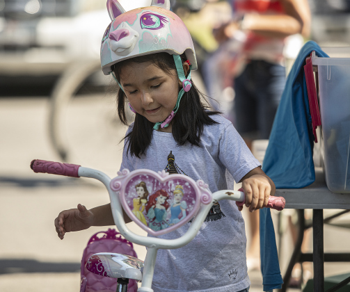 5-year-old Myra Shahi admires the bicycle given to her by  Georgetown Free Bikes, a non-profit that provides bicycles free of charge to those who need one (www.georgetownfreebikes.org) as she prepares to  ride in the Hometown Parade in San Gabriel Park on Thursday, July 4, 2024.  The Georgetown Sertoma Club sponsors the 4th of July Freedom Festival each year in San Gabriel Park.  Photo by Andy Sharp. 