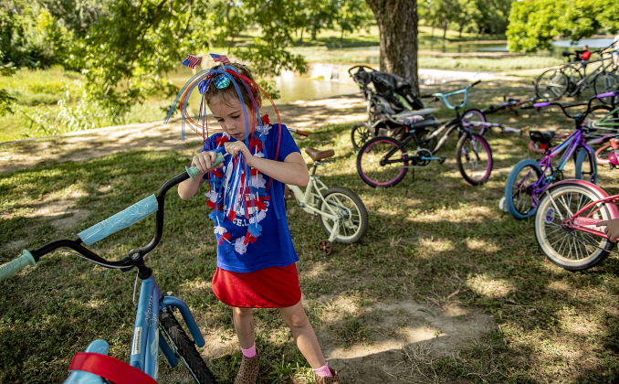 7-year-old Ellie Caputo gets her bike ready to go as she prepares to  ride in the Hometown Parade in San Gabriel Park on Thursday, July 4, 2024. Ellie received her bike today through Georgetown Free Bikes, a Georgetown non-profit that provides bicycles at no charge to those who want them (www.georgetownfreebikes.org). The Georgetown Sertoma Club sponsors the 4th of July Freedom Festival each year in San Gabriel Park.  Photo by Andy Sharp.