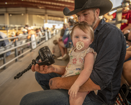 Bobby Herrmann uses a portable fan to keep his 8-month-old daughter Ophelia cool on a warm evening at the 74th Annual Taylor Rodeo on Thursday, July 18.