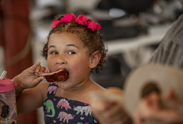 Three-and-a-half year old Nadzieja Komandosky sat alongside her grandfather Joseph Komandosky, one of the Ribs Category judges at  the 45th Taylor International BBQ Cook-Off on Saturday, August 17, 2024. Grandpa would sample some ribs, then share a little extra with Nadzieja, who seemed to enjoy the flavors a lot.    Held at Murphy Park, the event, attracting entrants from all over Texas, continued through Saturday.    Photo by Andy Sharp.