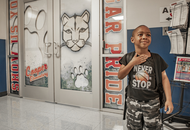 4-year-old Pre-k student Daniel Scott salutes during the Pledge of Allegiance at Cooper Elementary on Thursday morning, August 15, 2024,  the first day of school.  On the wall at left is a cougar, the school's mascot.  Cooper Elementary has 572 students enrolled this year.    Photo by Andy Sharp.
