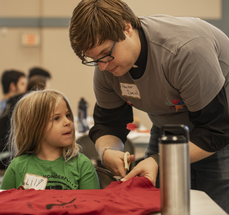 Reverend Drew Ingram, pastor at Christ Lutheran Church, assists his daughter Lily, 6, as they  create bags out of donated t-shirts during a 9/11 National Day of Service event held at Reverend Ingram's church  on Saturday, September 7, 2024.  Volunteers from churches, synagogues and mosques, including some who just wanted to contribute helped repurpose t-shirts to be used as bags at The Caring Place, Helping Hands of Georgetown and the Carver Center for Families.   Photo by Andy Sharp.
