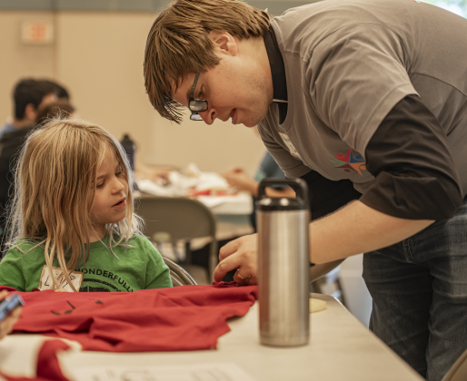 Reverend Drew Ingram, pastor at Christ Lutheran Church, assists daughter Lily, 6, as they  create bags out of donated t-shirts during a 9/11 National Day of Service event held at Reverend Ingram's church  on Saturday, September 7, 2024.  Volunteers from churches, synagogues and mosques, including some who just wanted to contribute helped repurpose t-shirts to be used as bags at The Caring Place, Helping Hands of Georgetown and the Carver Center for Families.   Photo by Andy Sharp.