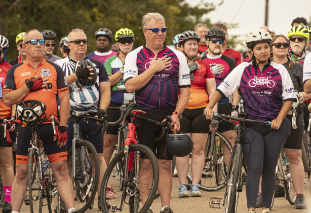 Cyclists taking part in a 25-mile ride pause while Terri Moore Mays sings "The Star-Spangled Banner" before their event begins  at Murphy Park for the annual Mamma Jamma Ride on Saturday, September 21, 2024.