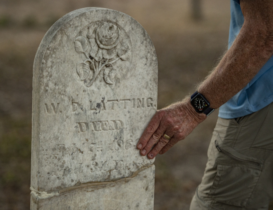 Joe Plunkett, with the Cemetery Restoration Volunteers, touches a gravestone his group restored  at the circa 1851 McFadin Cemetery on Tuesday, October 8, 2024. Plunkett and his group led the effort to restore this cemetery near the San Gabriel River in recent years.     Photo by Andy Sharp.  