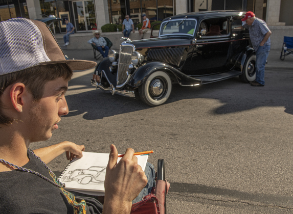 16-year-old Blake Mauldin sketches the 1934 Ford owned by his great-grandfather, 85-year-old Dennis McDaniel,  during Taylor's Main Street Car Show on Saturday, October 26, 2024. Mr. McDaniel is seen with the car in the distance.    Photo by Andy Sharp.