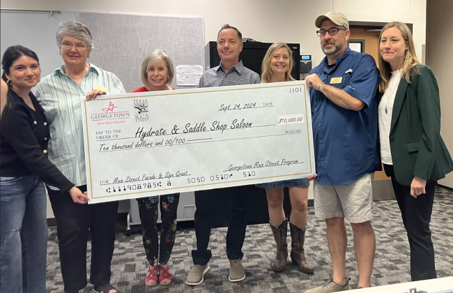 Business owners and main street board members pose with a ceremonial check. Hydrate &amp; Saddle Shop Saloon was awarded $10,000 as part of the Main Street Facade &amp; Sign Grant program.