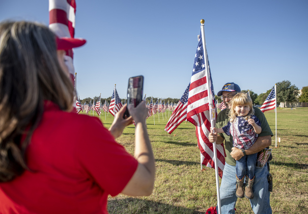 Field of Honor volunteer Tina McGuire, left, snaps a photo of Air Force veteran John Best and his two-and-a-half year-old grandson Lupe Durran-Best after John posted a flag honoring his father, veteran William Best, on Saturday, November 9, 2024, the official opening day of the Field of Honor.   Sponsored by the Rotary Club of Georgetown, the Field of Honor includes 2,000 American flags covering ten acres in San Gabriel Park.  With events throughout the week, the flags will fly here until November 17th.   P