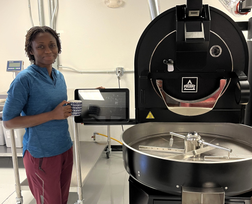 Mirian Diop, PhD, stands beside her coffee bean roaster with a cup of Tansania Ischesa coffee— a bean currently in the works.