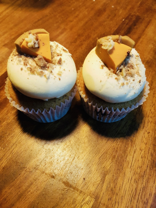 Two pumpkin-pie cupcakes have a decorative pie slice placed at the top. It’s a twist on the classic Thanksgiving dessert.