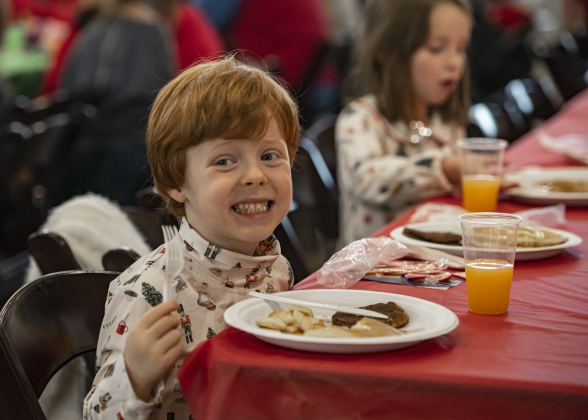 4-year-old Theo Hawkins, front, and his sister Rose, 5, back right, enjoy their pancakes, sausage and juice during Breakfast With Santa, held Saturday, December 21, 2024 at the San Gabriel Community Center.  The event, coordinated by the Georgetown Fire Department and the Rotary Club of Sun City, served up pancakes, sausage, juice and coffee too attendees.  Santa Claus was there throughout the morning to visit the kids and their families.    Photo by Andy Sharp.