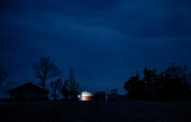 The early-evening blue night sky shines over a highlighted Texas flag along County Road 413 on Friday, January 3, 2025.