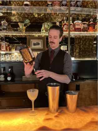 Brass Peacock Bar Manager Patrick Nikel serves a drink behind the bar. He’s crafted a menu of specialty cocktails, including the “Side Char,” which he is making here. Photo by Abbey Archer