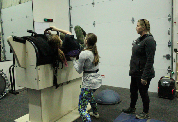 Emily Farley is assisted by Grace Beach to mount the vaulting barrel. Fly High Vaulters coach Samantha Kacir, right, watches for critique.