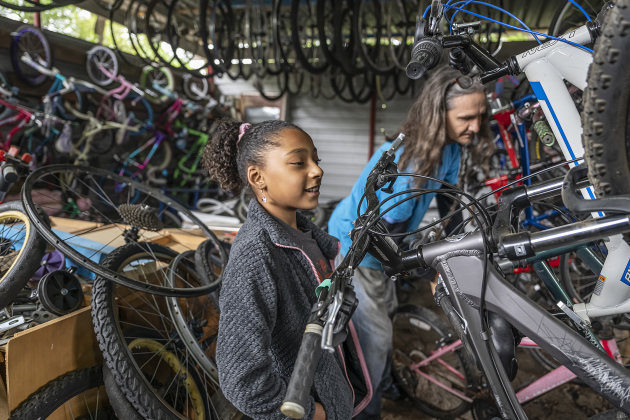 Ally Reyes, 9, is assisted by Thomas Holy as she selects a bicycle at Georgetown Free Bikes during the Grand Opening celebration of their new home on Saturday, April 5, 2025.