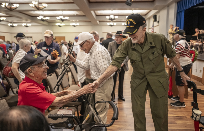 Navy veteran Bill Harper, 100, left, shakes hands with Army Special Forces veteran Robert ÒToo TallÓ Simmons, who will be 92 in June, at  the conclusion of the Memorial Day ceremony in Sun City on Monday, May 26, 2025. At center, holding the umbrella, is Korean War veteran Leonard Hummel, 92, who served in both the Navy and the Army.   Approximately 600 were in attendance.  Rain chances moved the event indoors.   Photo by Andy Sharp.
