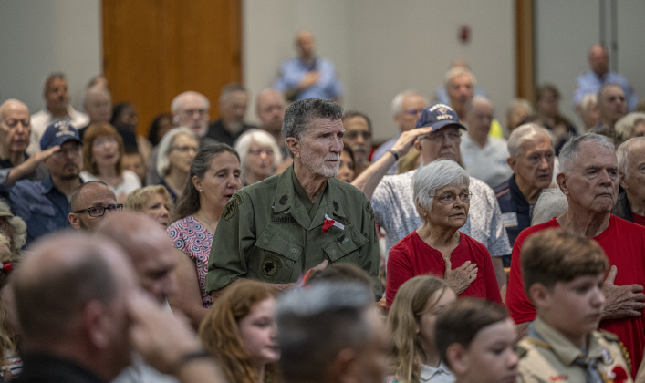 Army Special Forces veteran Robert “TooTall” Simmons, who will be 93 in June, stands with attendees for the playing of the National Anthem by the 36th Infantry Band during the Memorial Day ceremony in Sun City on Monday, May 26, 2025.  Approximately 600 were in attendance.  Rain chances moved the event indoors.   Photo by Andy Sharp.