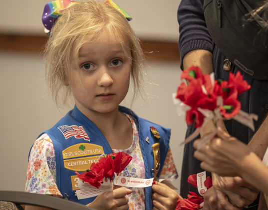 Girl Scout Laura Cieslak, 5, a member of Troop 317, was handing out traditional red poppies during  the Memorial Day ceremony in Sun City on Monday, May 26, 2025.  Approximately 600 were in attendance.  Rain chances moved the event indoors.   Photo by Andy Sharp.
