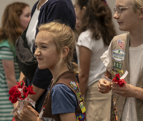 Julia Cieslak, 8, left, and her sister Katherine, 11, right,  members of Girl Scout Troop 317,  helped distribute traditional red poppies during the Memorial Day ceremony in Sun City on Monday, May 26, 2025.  Approximately 600 were in attendance.  Rain chances moved the event indoors.   Photo by Andy Sharp.