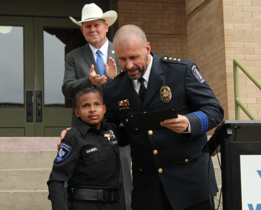 After being sworn in as an honorary officer, Chief Tchida presents DJ with a plaque with his Police ID and hugs him.