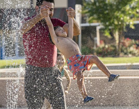 Jose Rogel swings his son Maximillian, 4, through the water while daughter Luna, 5, looks on  during a visit to the splash pad at Heritage Square Park on Tuesday, June 17, 2025.  The official beginning of summer is Friday, June 20th, but Williamson County residents have been seeking respite for a while.